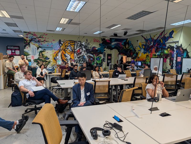 StartupA2Z attendees listening beside Hacker Dojo’s founder mural